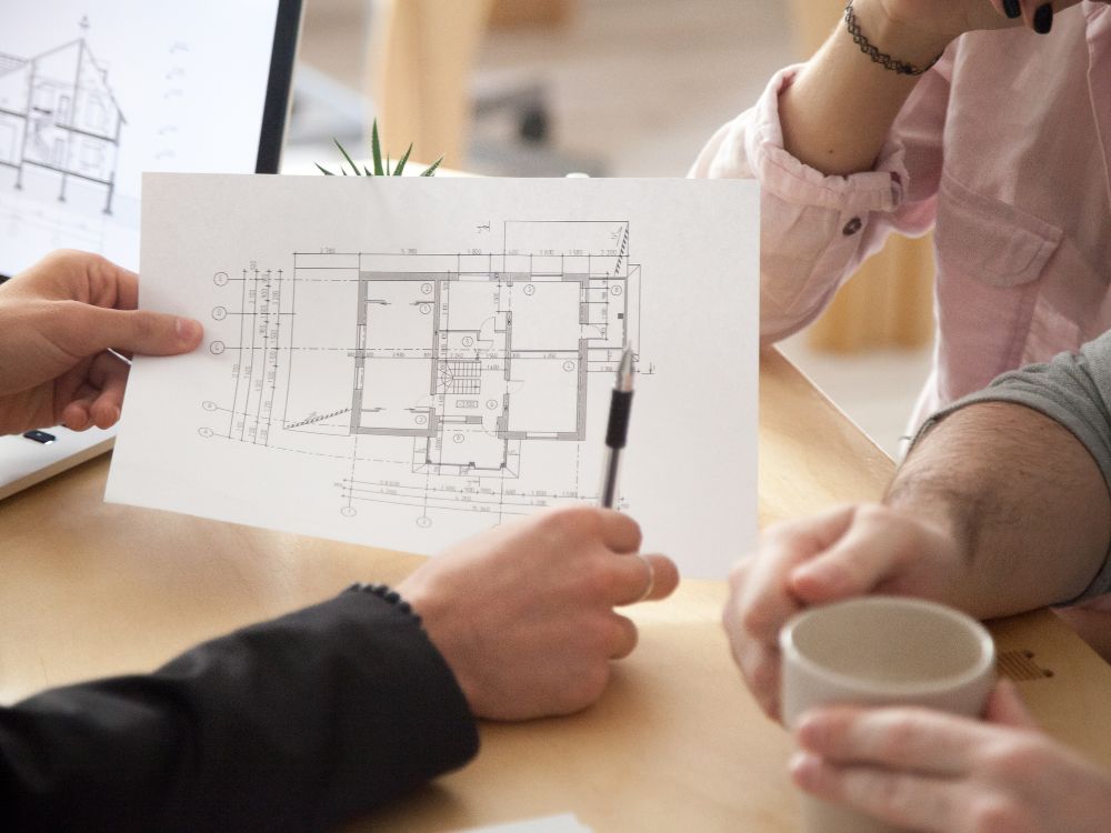 Profissionais discutindo uma planta arquitetônica em uma reunião de planejamento, etapa importante para quem vai financiar apartamento na planta.