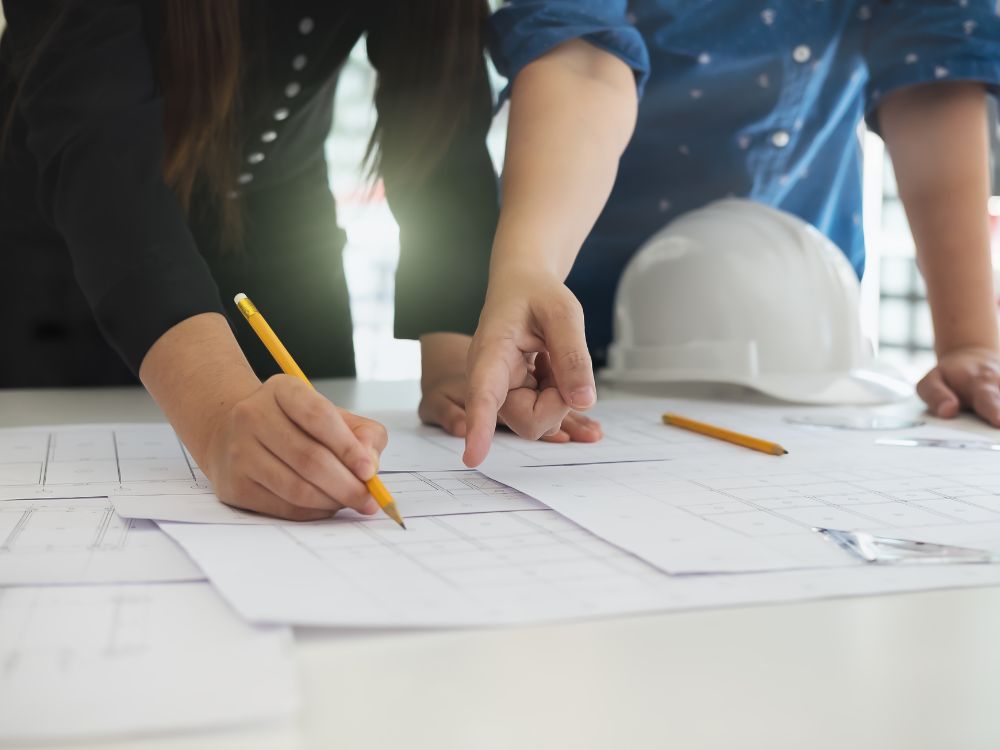 Mãos de engenheiros revisando projetos imobiliários em um escritório, garantindo que todas as etapas do financiamento de apartamento na planta sejam seguras.