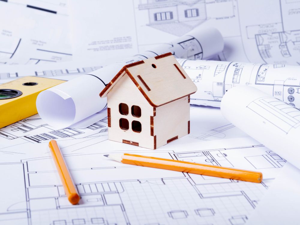 Miniatura de casa sobre projetos de construção, representando o conceito de como comprar apartamento na planta com planejamento.