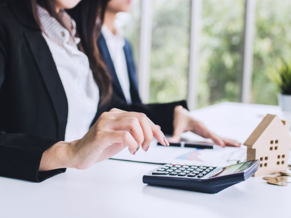 Mulher calculando valores para financiamento imobiliário com miniatura de casa na mesa. Quanto preciso dar de entrada para financiar um apartamento?