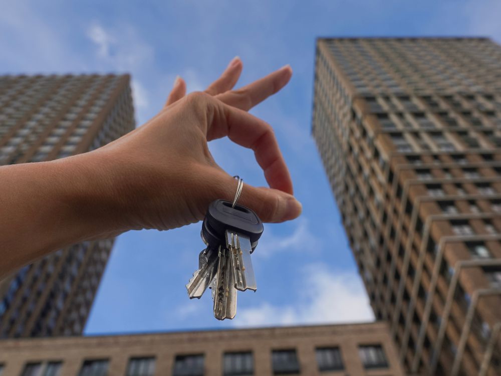 Mão segurando chaves de apartamento com edifícios ao fundo. Quanto preciso dar de entrada para financiar um apartamento?