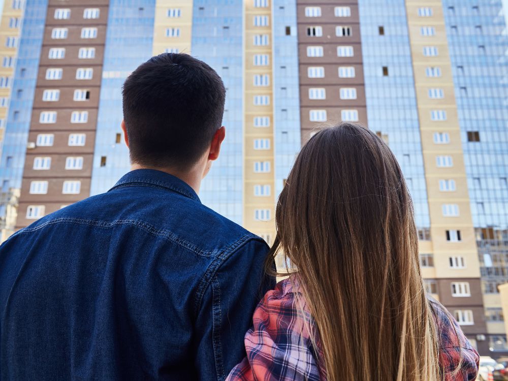 Casal observando prédio residencial recém-construído e refletindo sobre as implicações de morar antes do Habite-se na regularização do imóvel.