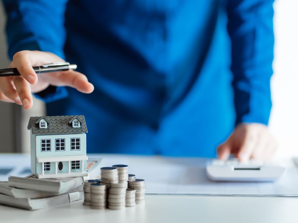 Pessoa com miniatura de casa e moedas simbolizando planejamento financeiro para investir em Joinville com foco em rentabilidade.