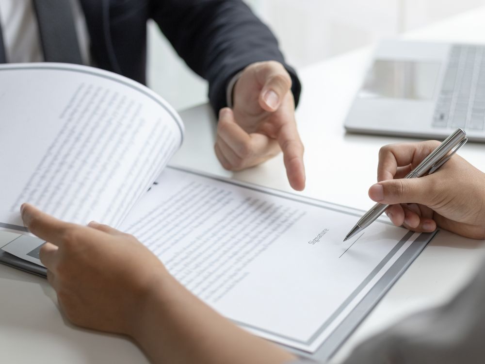 Pessoa assinando contrato imobiliário com orientação de corretor para esclarecer dúvidas sobre habite-se demora quanto tempo.