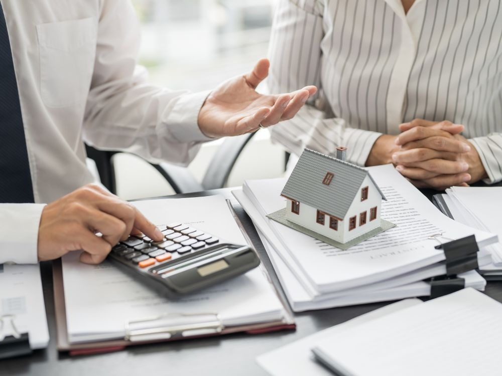 Corretores analisando documentos e calculadora sobre mesa, ilustrando o planejamento financeiro antes de comprar apartamento para investimento.