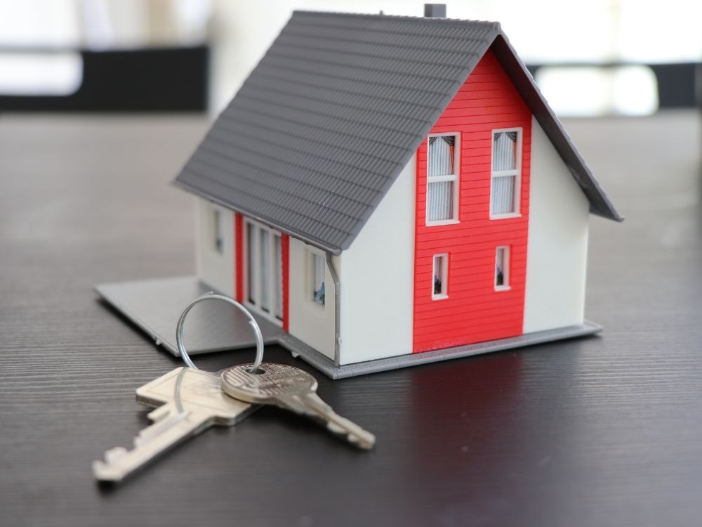 Casa em miniatura com chaves sobre a mesa, representando compra e propriedade. Imóvel é um bom investimento? Entenda agora!