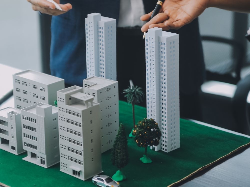 Profissionais analisando uma maquete urbana com prédios e áreas verdes, ilustrando estudo de projetos e valorização de imóvel em regiões em desenvolvimento.