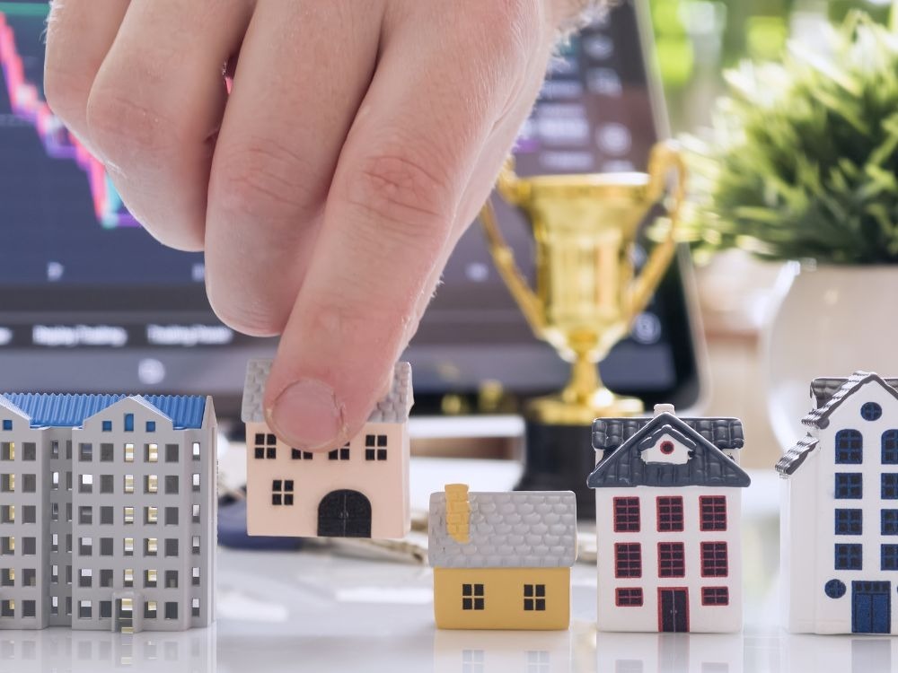 Miniaturas de casas alinhadas enquanto uma mão seleciona um dos modelos, representando análise e valorização de imóvel no mercado imobiliário.