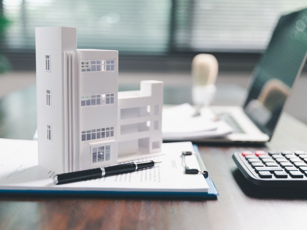 Maquete de edifício sobre documentos, caneta e calculadora, simbolizando planejamento financeiro e valorização de imóvel por meio de avaliação técnica.