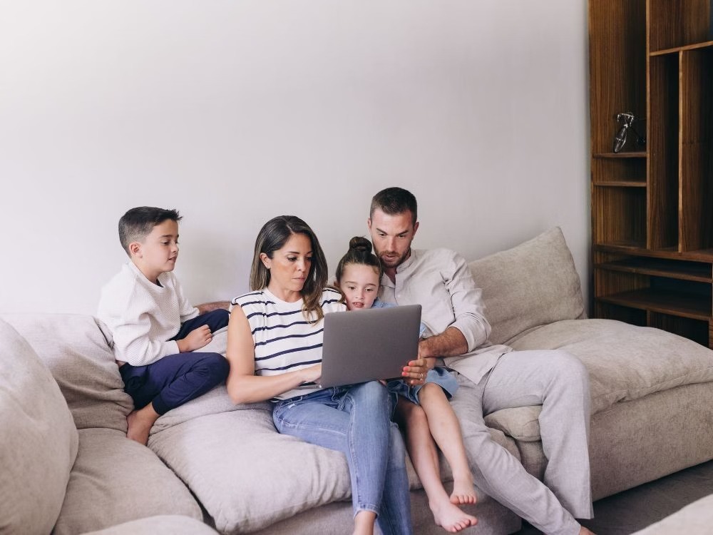 Família reunida no sofá analisando opções de compra no computador, cenário comum ao pesquisar Como usar o FGTS para comprar um imóvel.