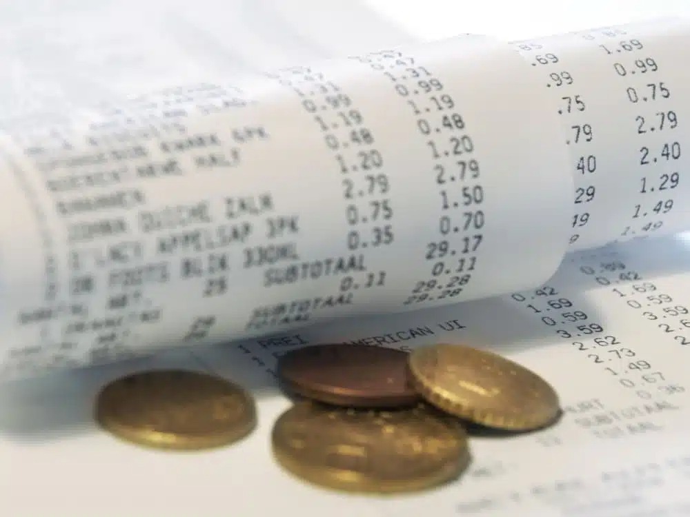 Nota fiscal com moedas sobre a mesa, representando despesas do dia a dia e ajudando a entender qual o custo de vida em Joinville.