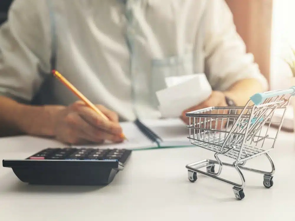 Pessoa calculando despesas com carrinho de compras em miniatura, simbolizando planejamento financeiro e qual o custo de vida em Joinville.