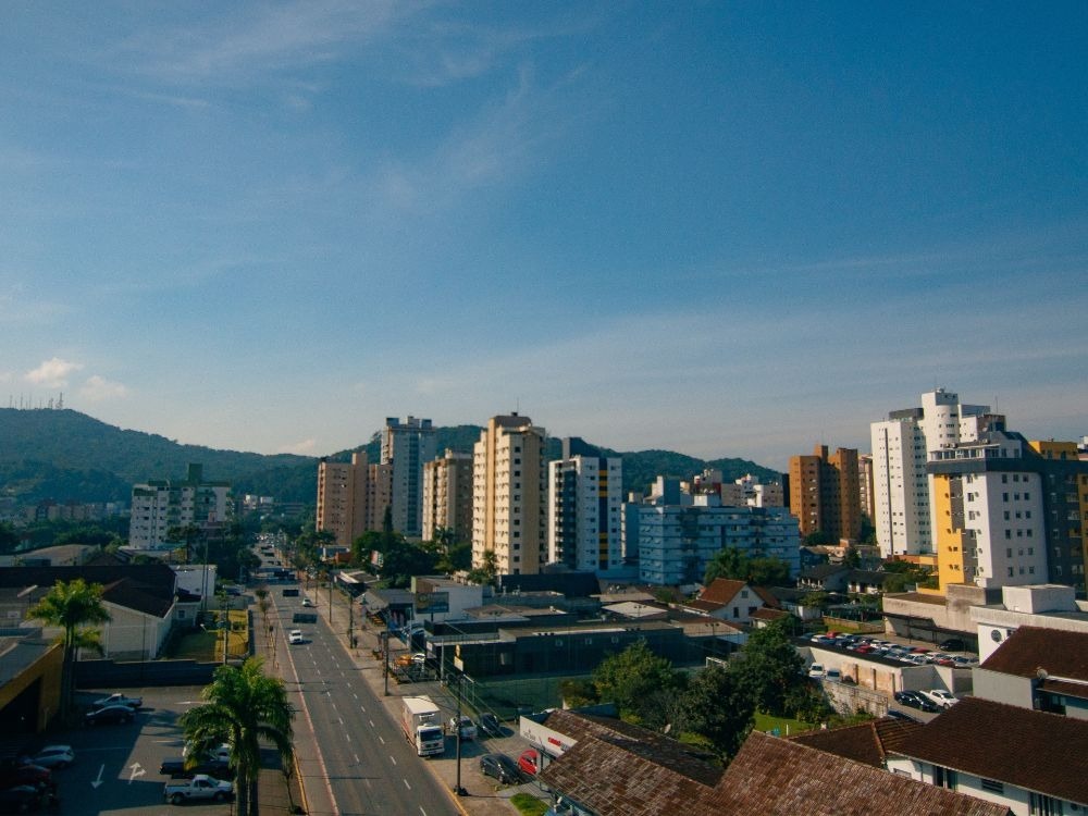 Avenida urbana com prédios residenciais e comércio, ilustrando a infraestrutura e qual o custo de vida em Joinville.
