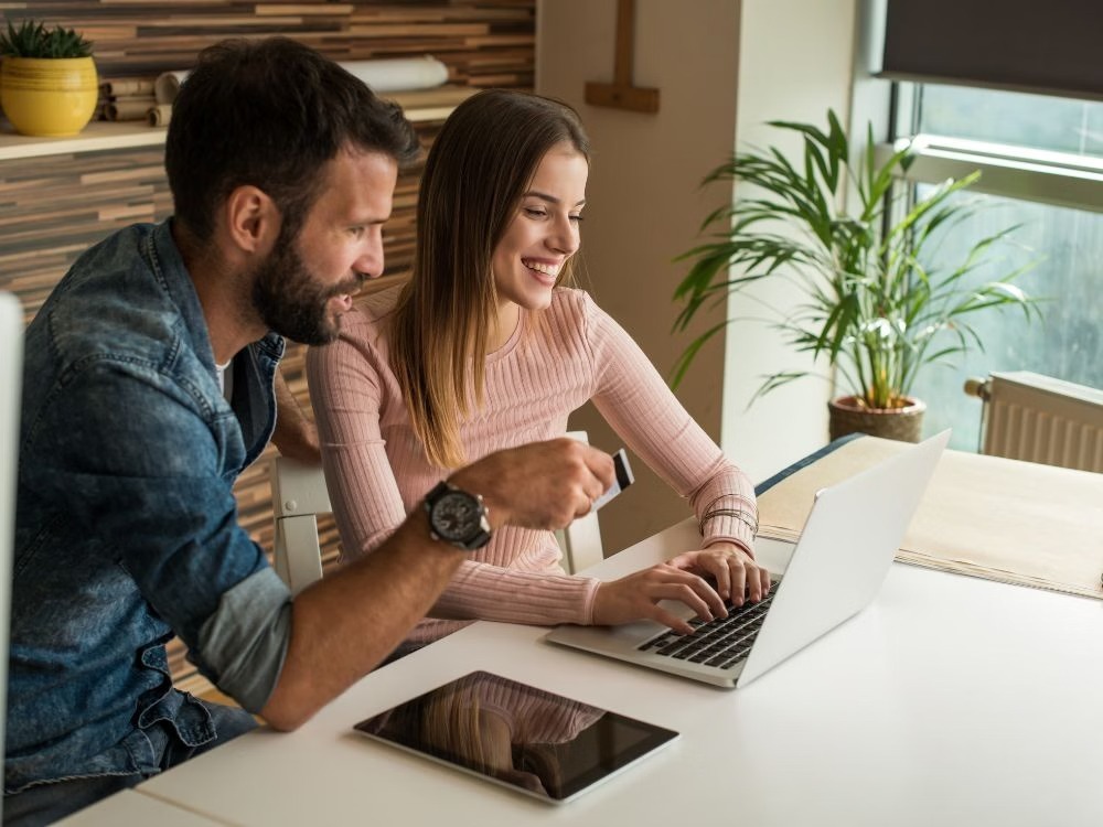Casal avaliando informações no notebook durante planejamento financeiro, relacionado a dúvidas sobre Como usar o FGTS para comprar um imóvel.