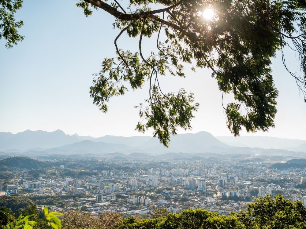 Vista panorâmica urbana cercada por montanhas e áreas verdes, representando as Melhores cidades para investir em imóveis no Brasil.