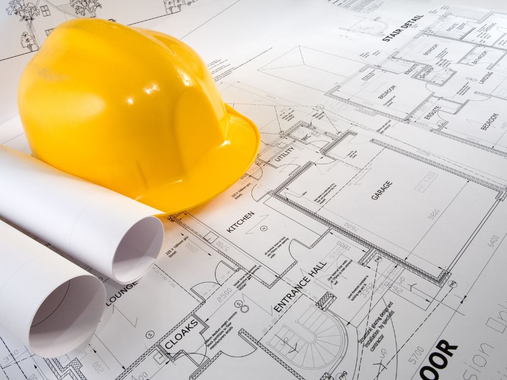 Capacete de obra sobre planta arquitetônica ilustrando qual a diferença entre construtora e incorporadora em projetos imobiliários.