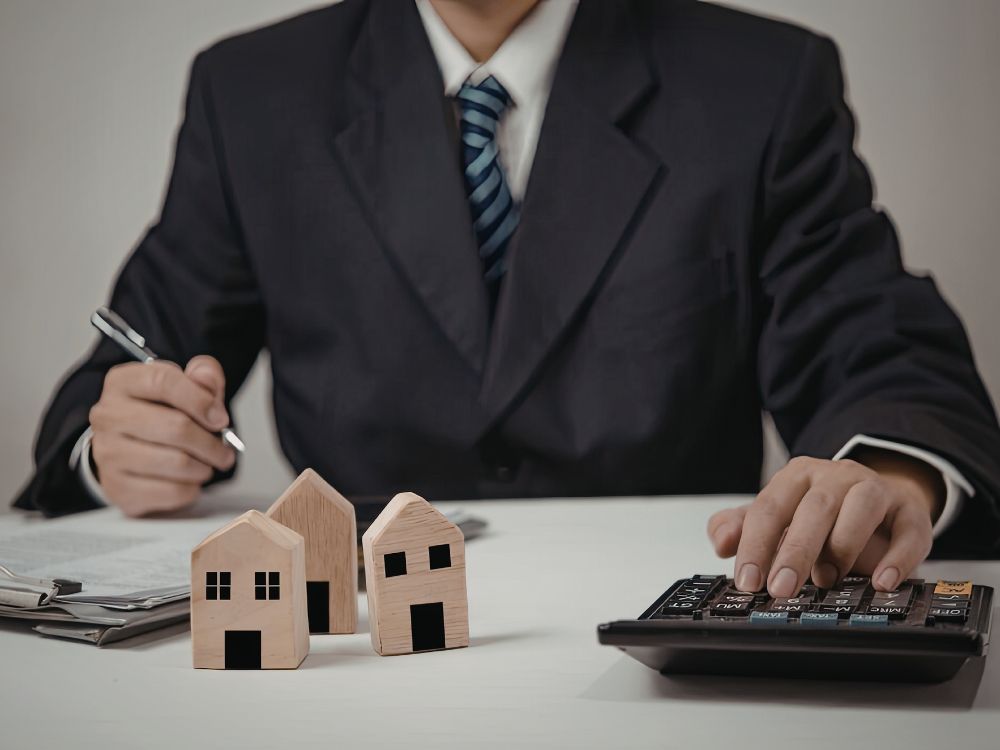 Profissional calculando custos com miniaturas de casas explicando qual a diferença entre construtora e incorporadora no mercado imobiliário.