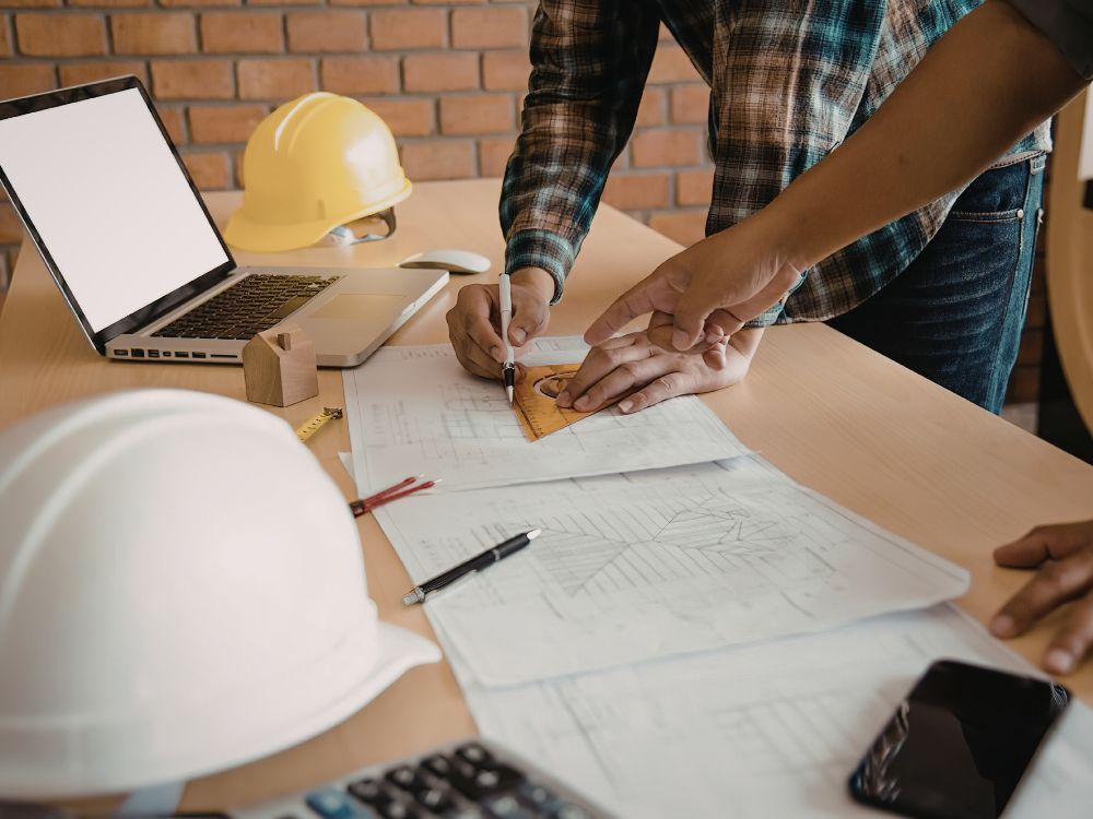 Profissionais analisando planta com notebook mostrando qual a diferença entre construtora e incorporadora na prática