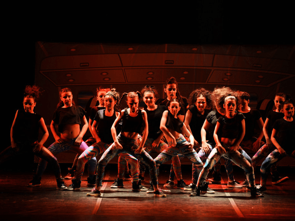 Grupo de jovens dança coreografia de estilo urbano em palco iluminado durante apresentação no Festival de Dança de Joinville.
