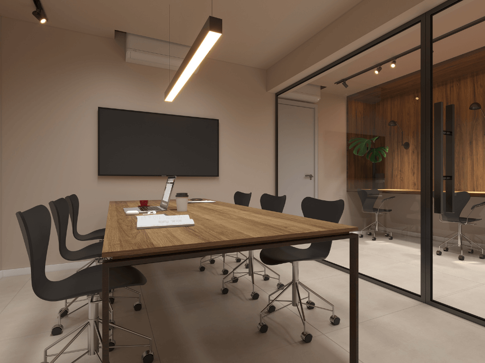 Sala de trabalho moderna com mesa ampla, cadeiras, iluminação planejada e divisória de vidro em um ambiente corporativo. Tudo para explicar o que é Wellness Real Estate