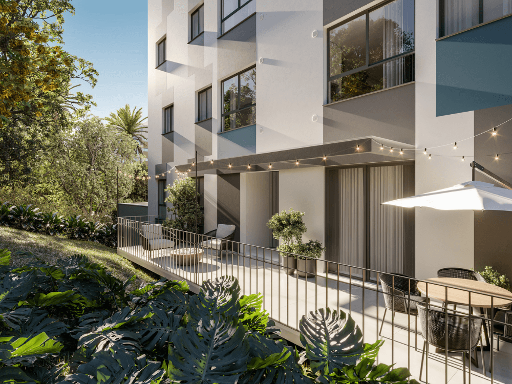 Fachada de edifício residencial com varanda mobiliada, plantas ornamentais e área externa que valoriza o imóvel para investimento.