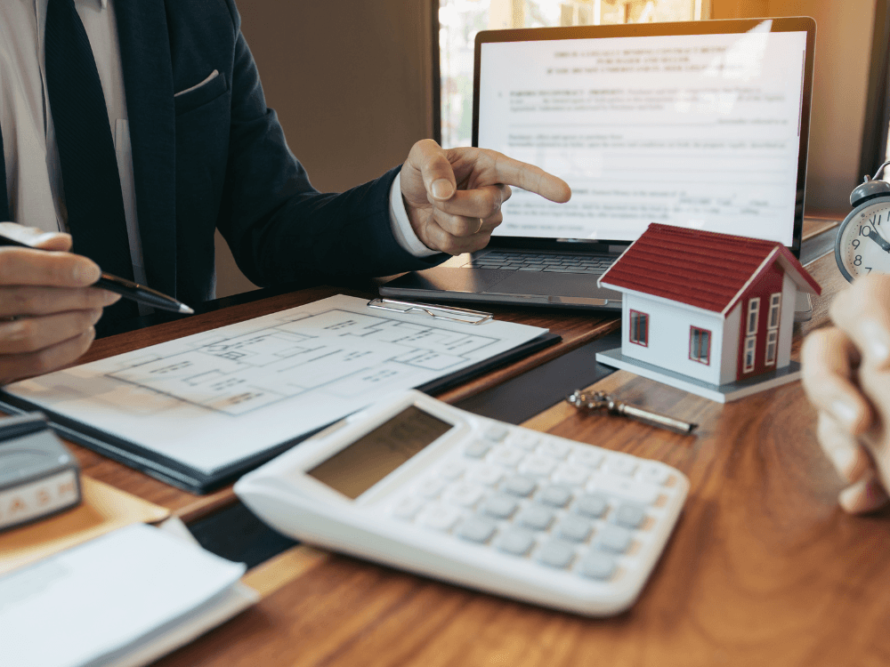 Profissional analisa documentos de um imóvel com calculadora e maquete de casa durante uma negociação imobiliária em Joinville.