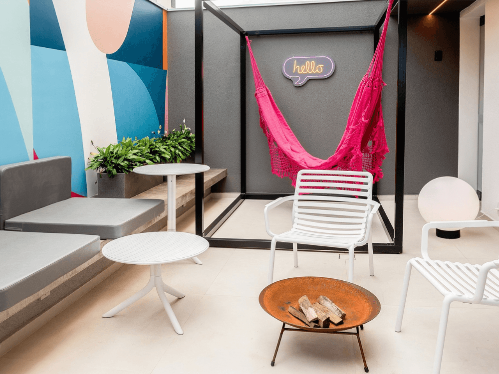 Área de convivência com jardim, poltronas, mesas e rede em empreendimento residencial, tendência imobiliária em Joinville. Tudo para explicar sobre as tendências do mercado imobiliário.