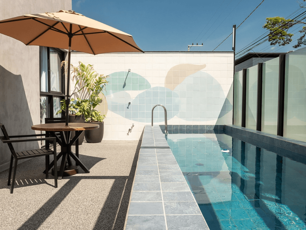 Piscina residencial ao ar livre com mesa, guarda-sol e plantas, mostrando uma área de lazer valorizada em Joinville.